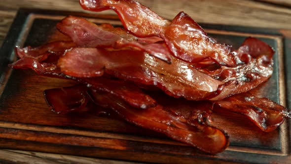 Super Slow Motion Shot of Roasted Bacon Slices Falling on Wooden Board at 1000 Fps. alt