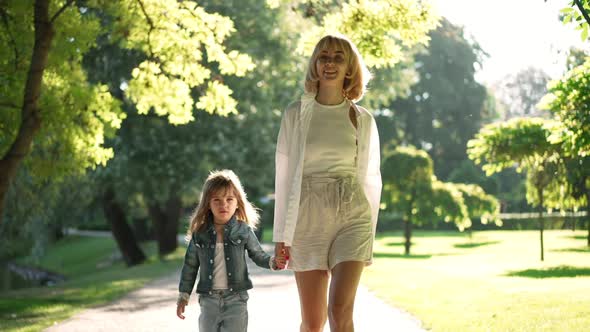 Dolly Shot of Happy Smiling Woman and Girl Walking in Sunshine Holding Hands Talking alt