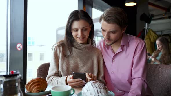 Excited Couple Reading Good News on Mobile Phone Sitting in a Coffee Shop