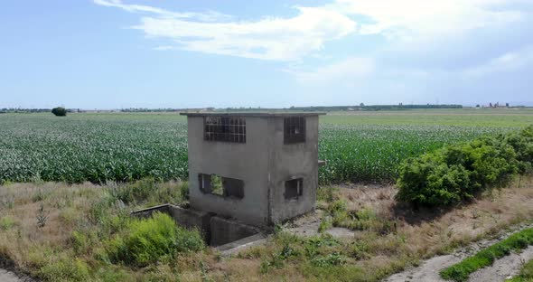Old And Abandoned Concrete Building At Corn Fields In Countryside On A Sunny Day. - aerial alt