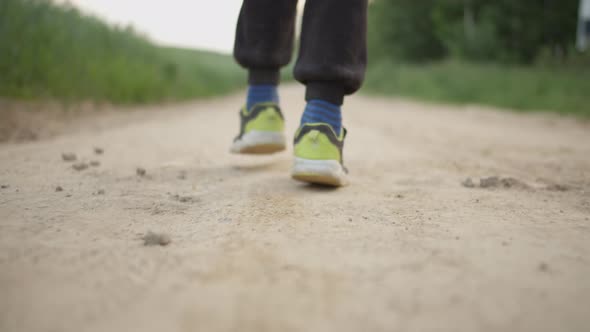 Closeup of a Boy's Dirty Feet Walking Along a Country Road Near the Field Back View