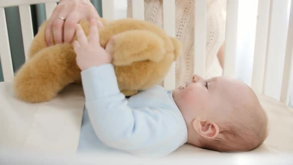 Happy Smiling Baby Boy Palying and Holding Teddy Bear While Lying in Wooden Cradle alt