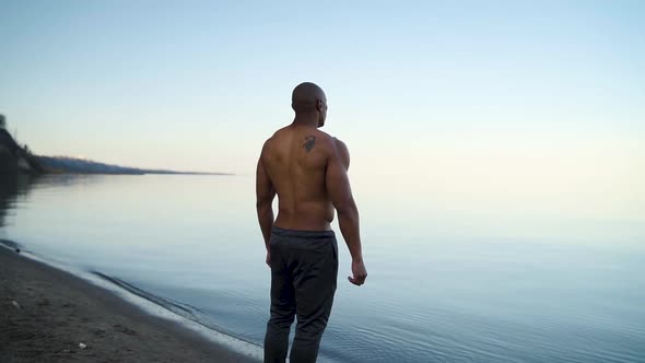Athletic man looking out across the water on a beach in slow motion alt