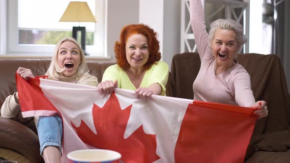 Joyful Female Hockey Fans Cheering Sitting in Living Room Indoors Watching Match on TV alt