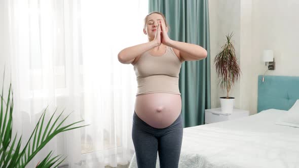 Happy Smiling Pregnant Woman with Big Belly Standing at Big Window and Doing Yoga Exercises and alt