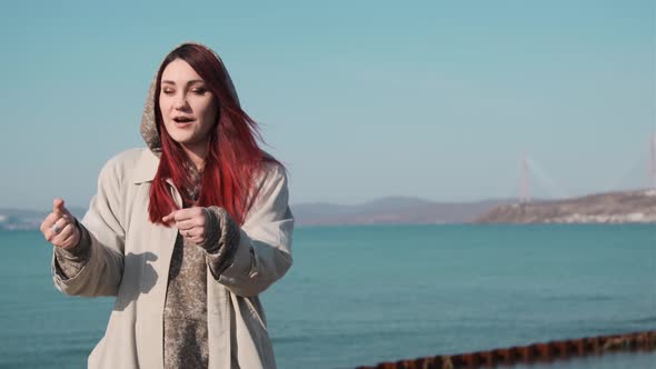 one girl in a coat stands on the shore of a calm sea