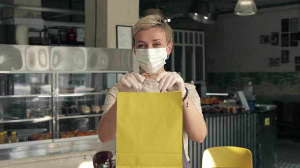 Waitress in Mask and Gloves Holding Bag with Mealtogo alt