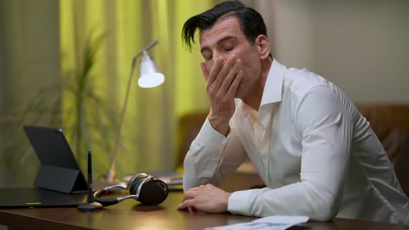 Troubled Middle Eastern Young Man Rubbing Face Thinking Sitting at Table in Home Office alt