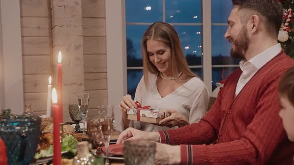 Man Giving Her Wife a Gift at the Table on Christmas Eve Everybody Smiling alt