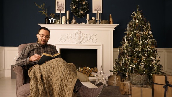Portrait of a man reading book to the camera on Christmas evening. alt