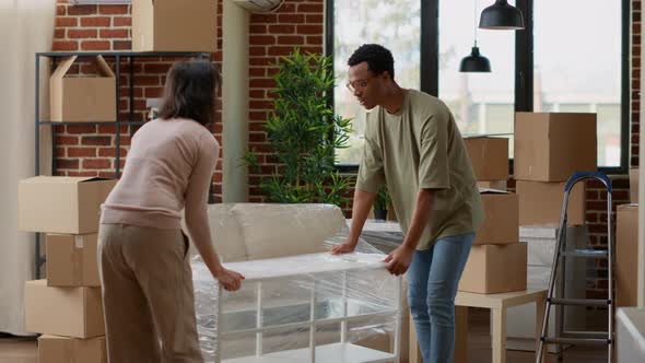 Multiethnic Partners Carrying Table in New Rented Home alt