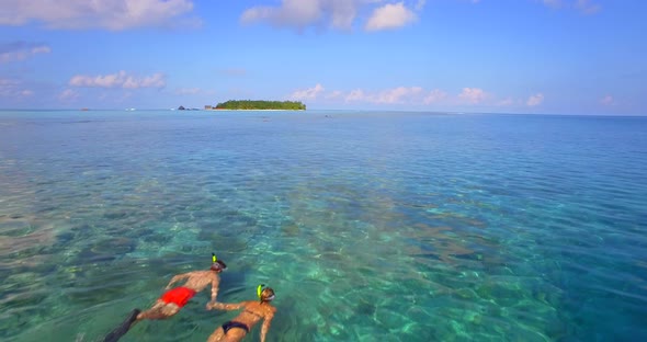 Aerial drone view of a man and woman couple snorkeling over the coral reef of a tropical island. alt