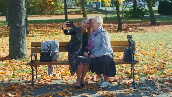 Zoom Shot of Young and Old Women Making Selfie on Smartphone in Autumn Time in a Beautiful Park alt