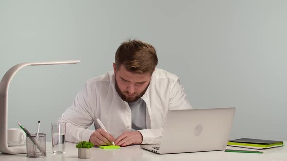 Serious Young Man Sitting at Desk in Home Office Taking Notes Working Remotely alt
