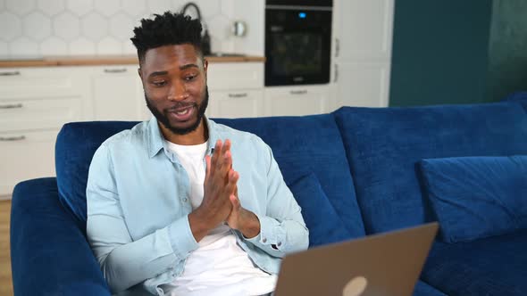 Smiling Young Bearded Man Sitting on the Couch with Laptop on His Lap Videocalling alt