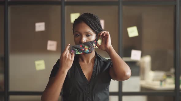 Young African Businesswoman Stands in Conference Room, Woman Puts on a Cloth Mask To Protect Himself alt