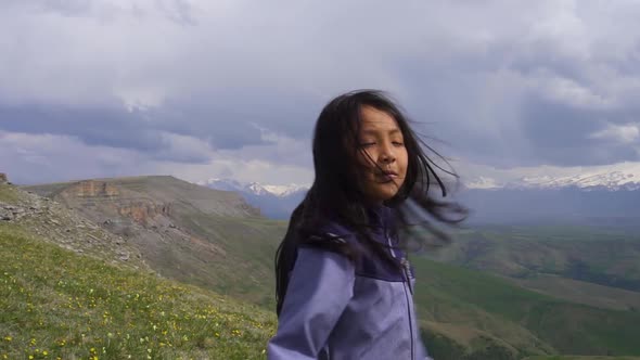Little Asian Girl Spinning in the Wind on a Background of Mountains