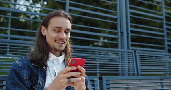 Crop View of Happy Millennial Guy with Long Hair Laughing While Using Smartphone, Bearded Young Man alt