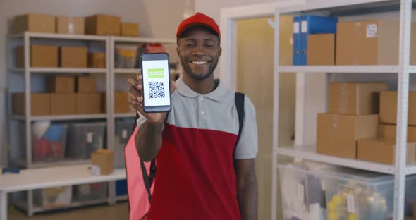 Happy Afroamerican Deliveryman Smiling at Camera Showing Cellphone with Vaccinated Qrcode alt