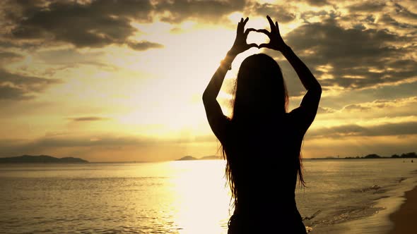 Silhouette, a heart-shaped hand-made woman around the sun in the evening by the sea.