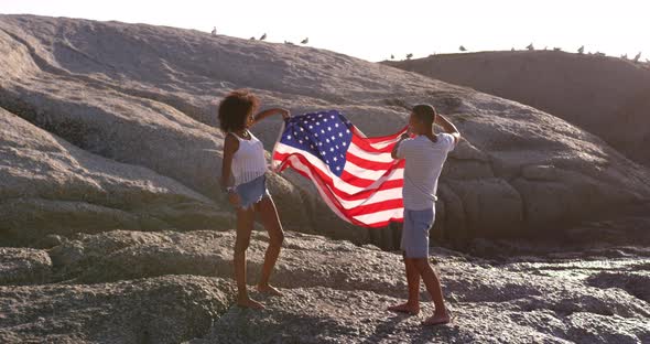 Couple holding American flag on rock at beach in the sunshine 4k