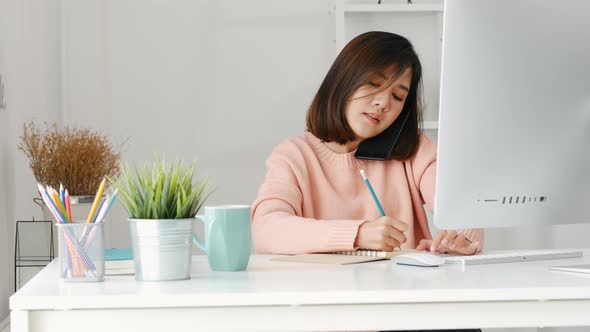 Young beautiful Asian woman talking with smart phone and using computer desktop at the home office. alt