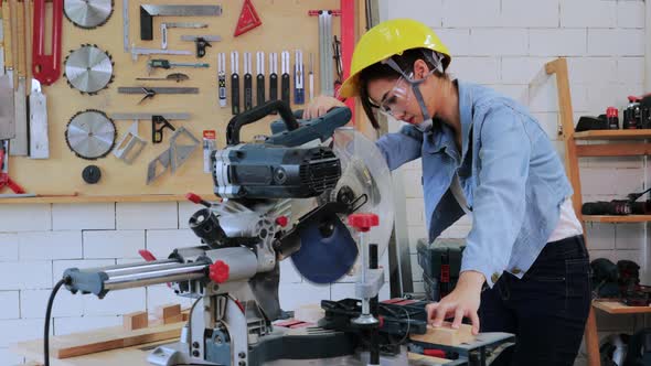 Asian carpenter student woman in safety suit cutting machine in university wood workshop