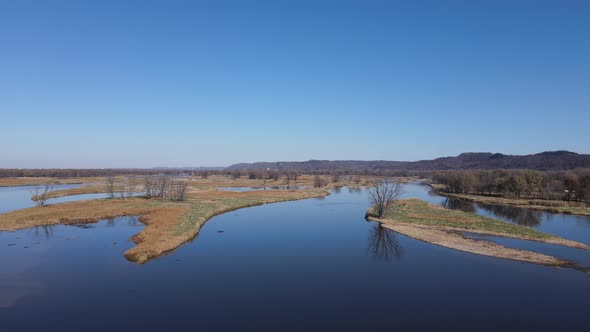 Wide aerial view of river with small islands of land with trees. Bluffs in the background.