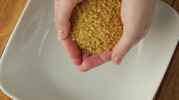 Closeup of a Woman's Hands Spilling Out Dried Yellow Bulgur Wheat Grains Into a Plate Slow Motion alt