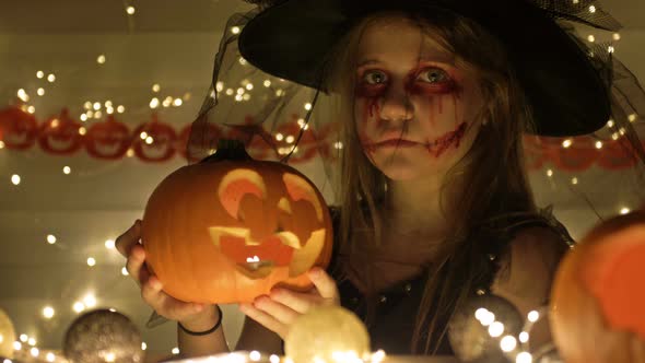 Portrait of a Teenage Girl Dressed As a Witch with Scary Makeup on Her Face. The Girl Holds a Jack-o alt