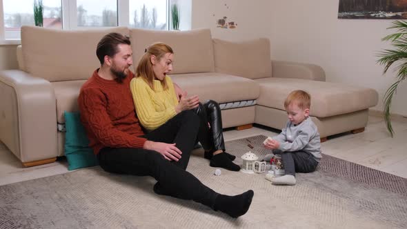 Happy Young Parents are Smiling Hugging and Playing with Their Little Son alt