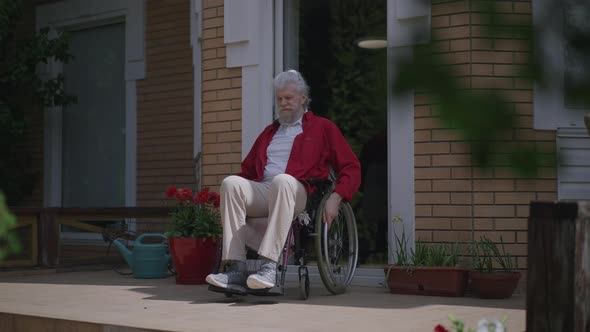 Positive Bearded Disabled Man Rolling Wheelchair on Porch in Slow Motion Admiring Sunlight Outdoors alt