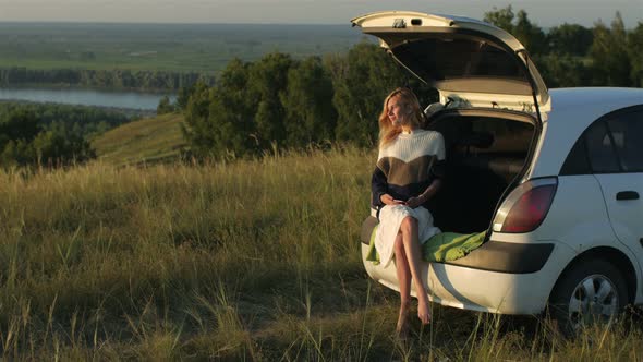 beautiful young woman resting in the trunk of a car on a cliff