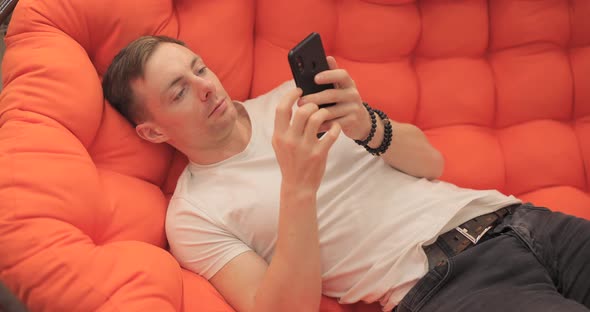 Man Looking at Photos on the Phone While Lying on the Couch