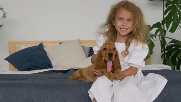 little cute blonde girl play with cocker spaniel puppy on a bed
