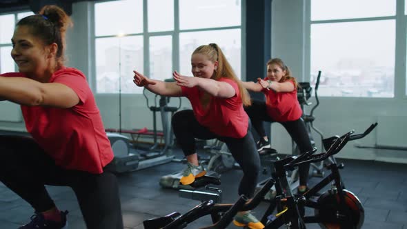 Group of Smiling Friends Women Class Exercising Training Spinning on Stationary Bike at Modern Gym alt