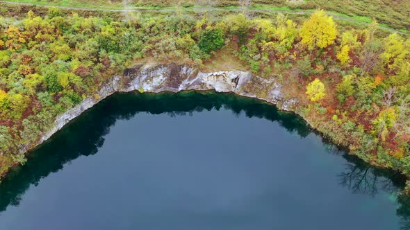 A top down view over a quarry filled with green water. The camera slowly dolly in while tilted down alt