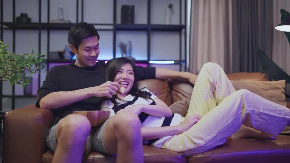 Asian sweet couple watching tv relax sitting on sofa in living room at home