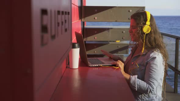 Happy Woman with Yellow Headphones Has Videocall on Laptop