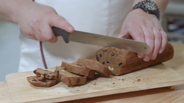 Baker is Cutting Baked Dutch Bread with Raisins and Dried Apricots with Knife alt