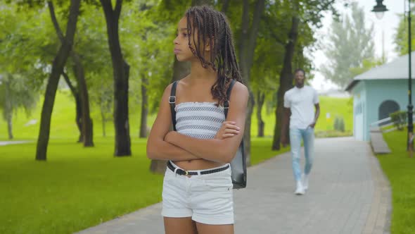 Portrait of Charming African American Girl Waiting Brother in Summer Park. Cute Sister with Pigtails alt