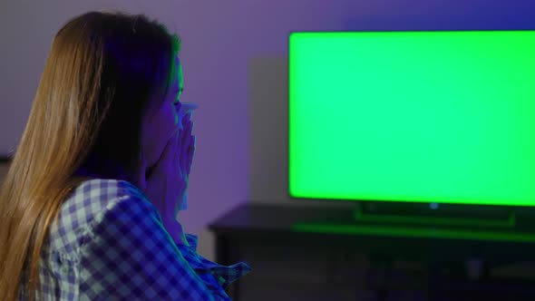 Young Woman Sits on an Armchair and Watches TV