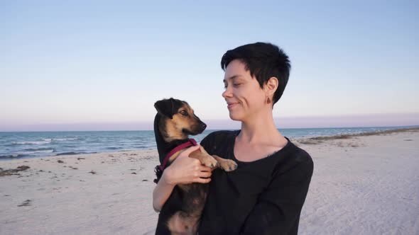 Girl carries her dog, walking along the beach near the sea.