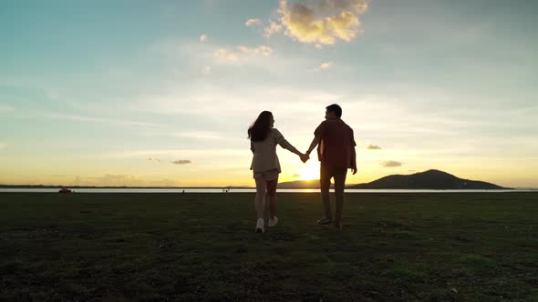 slow-motion of young couple holding hands walking in green field at sunset
