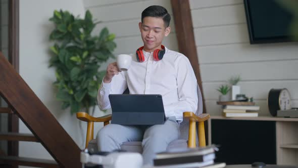 Front View Portrait of Cheerful Handsome Young Asian Man Drinking Morning Coffee in Living Room alt