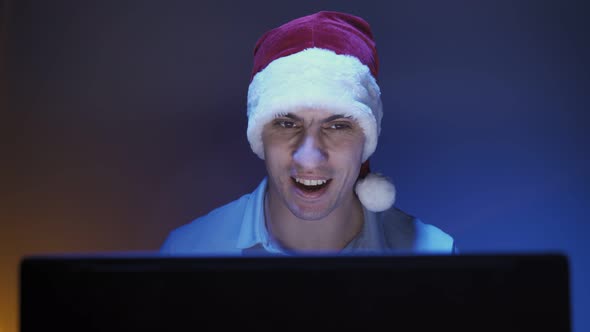 Happy Man in Santa Claus Hat Smiles and Communicates on Video Call Using Laptop alt