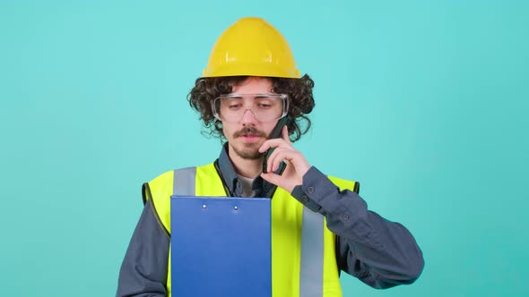 Construction Worker with Safety Glasses and Helmet That is Talking on Mobile Phone alt