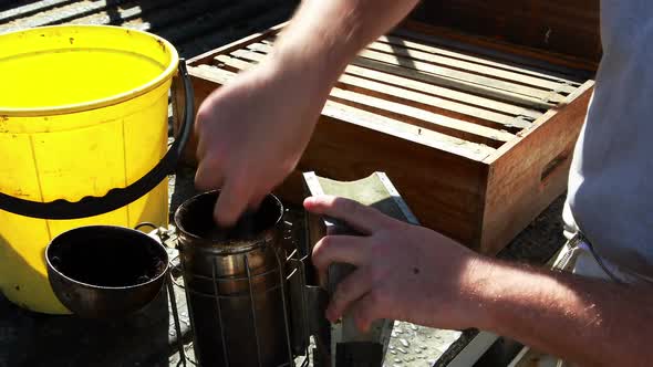 Beekeeper preparing smoker for harvesting in apiary alt