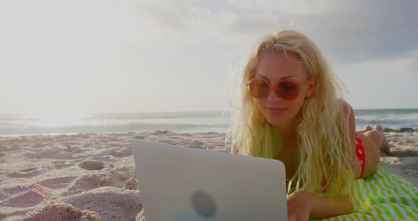 Woman in bikini and sunglasses using laptop on beach 4k