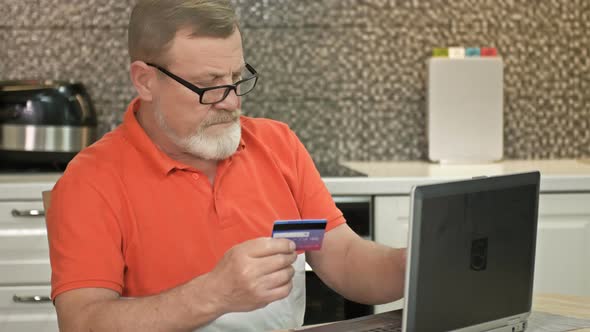 Senior Man at Laptop Paying with Bank Card for Online Shopping alt